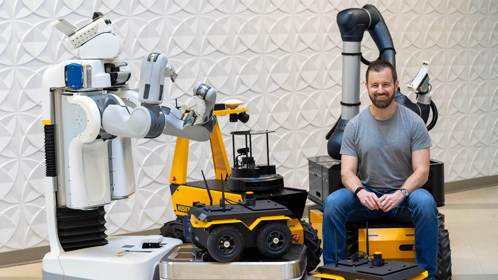 Ryan Gariepy sits smiling with robots.