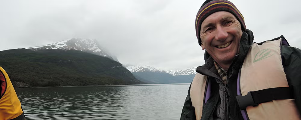 Dr. Neil Thomson on a boat with mountains in the background.