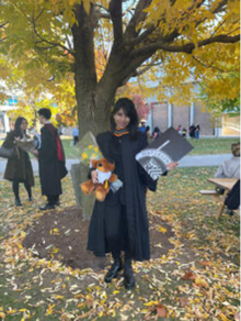 Maria Shamim in convocation regalia holding her diploma.