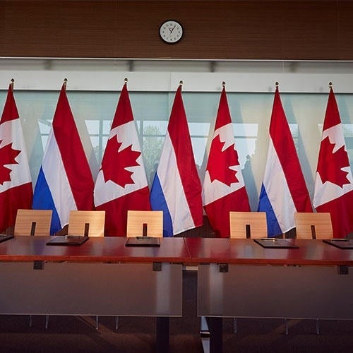 A table and chairs set up with alternating Canadian and Dutch national flags behind.