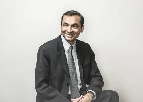 Sushanta Mitra in suit, smiling against blank wall