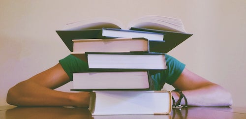 A person is hidden behind a stack of textbooks.