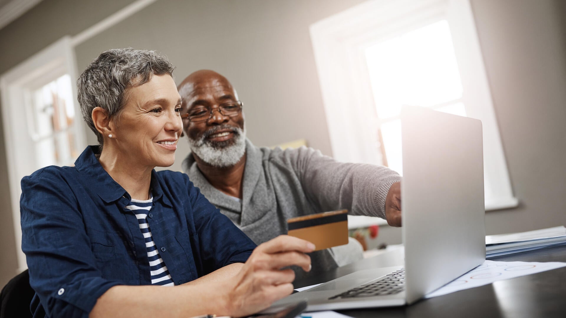 A woman holding a credit card and a man, both at a computer.