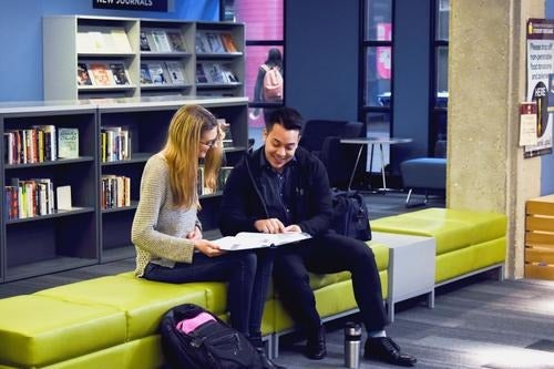 Two students in the library looking at a textbook