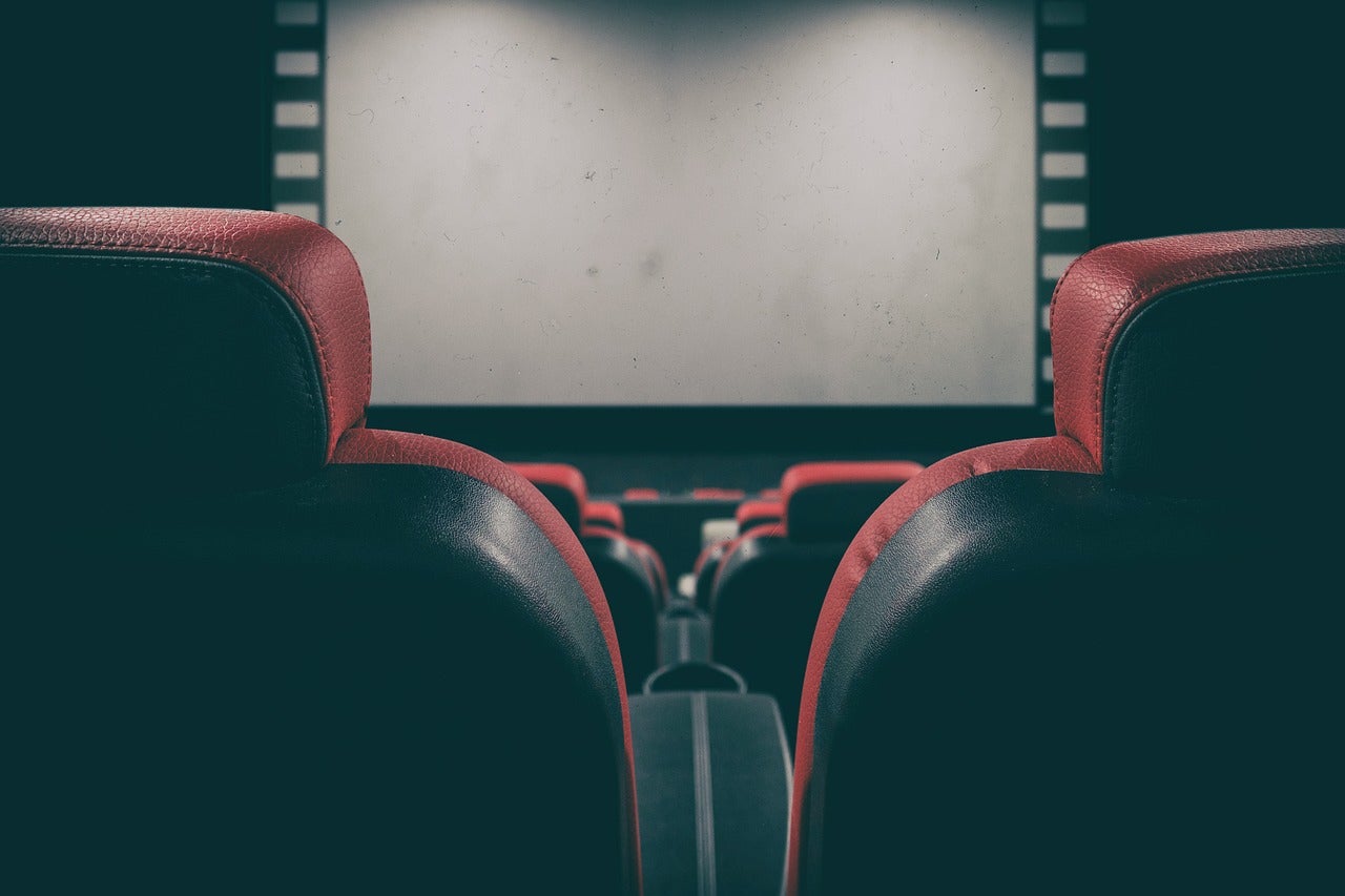 A photo of movie theatre seats with the screen in the background.