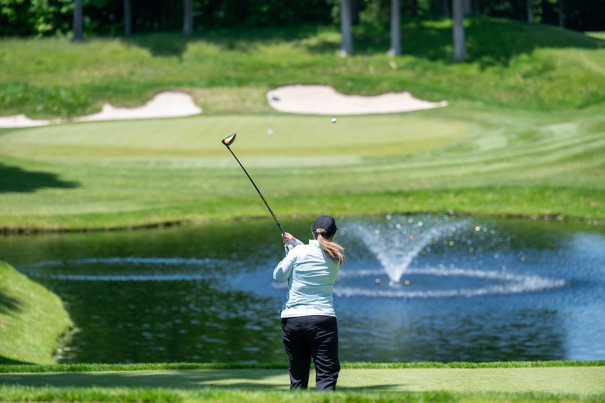A golfer sends her drive over a pond towards the green.