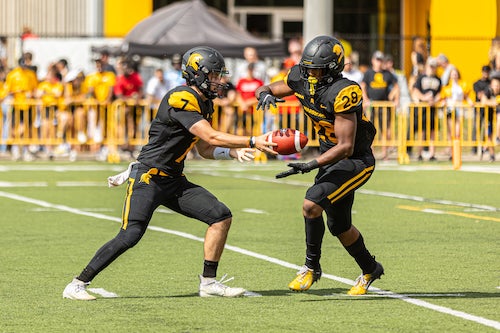 Anthony Miller hands a football off to Nolan Kaban during a Warriors game.