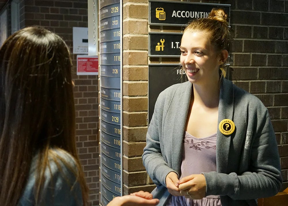 A volunteer wearing a &quot;here to help&quot; button gives directions to a new student.