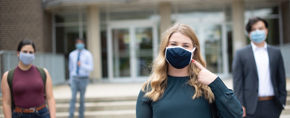 A student wearing a mask and a smile with a few other masked students standing behind her.