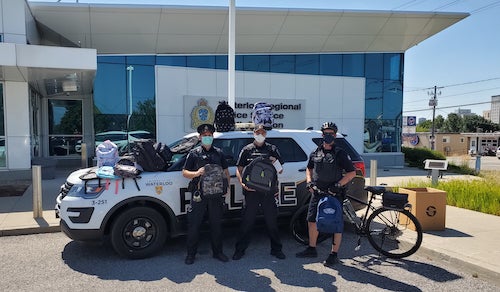 Three members of Campus Police show off the donated backpacks as they drop them off at Waterloo Police Headquarters.