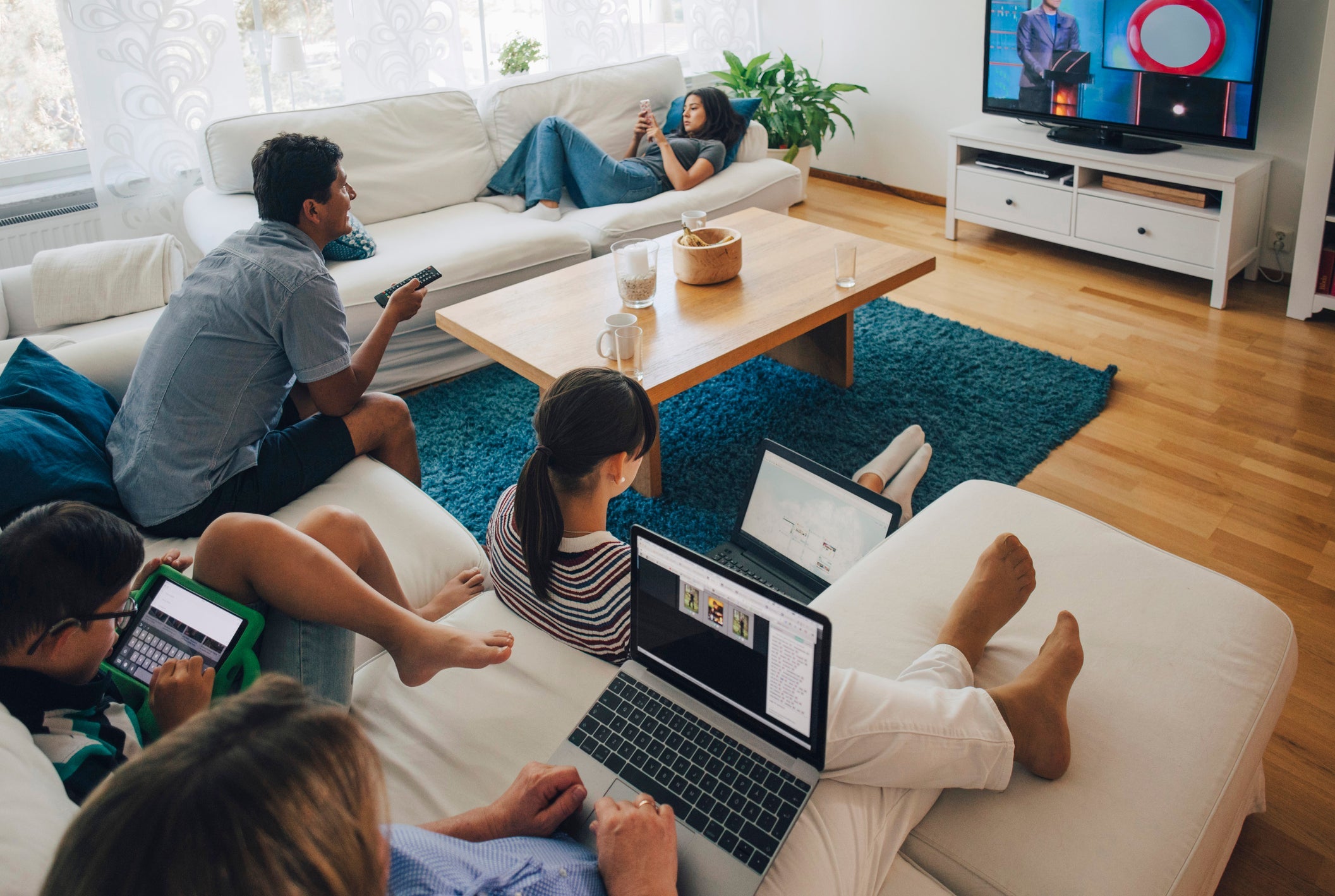 Family members sit on couches while engrossed in their own digital devices.