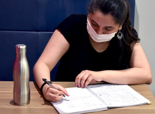 A masked woman writes in a notebook.