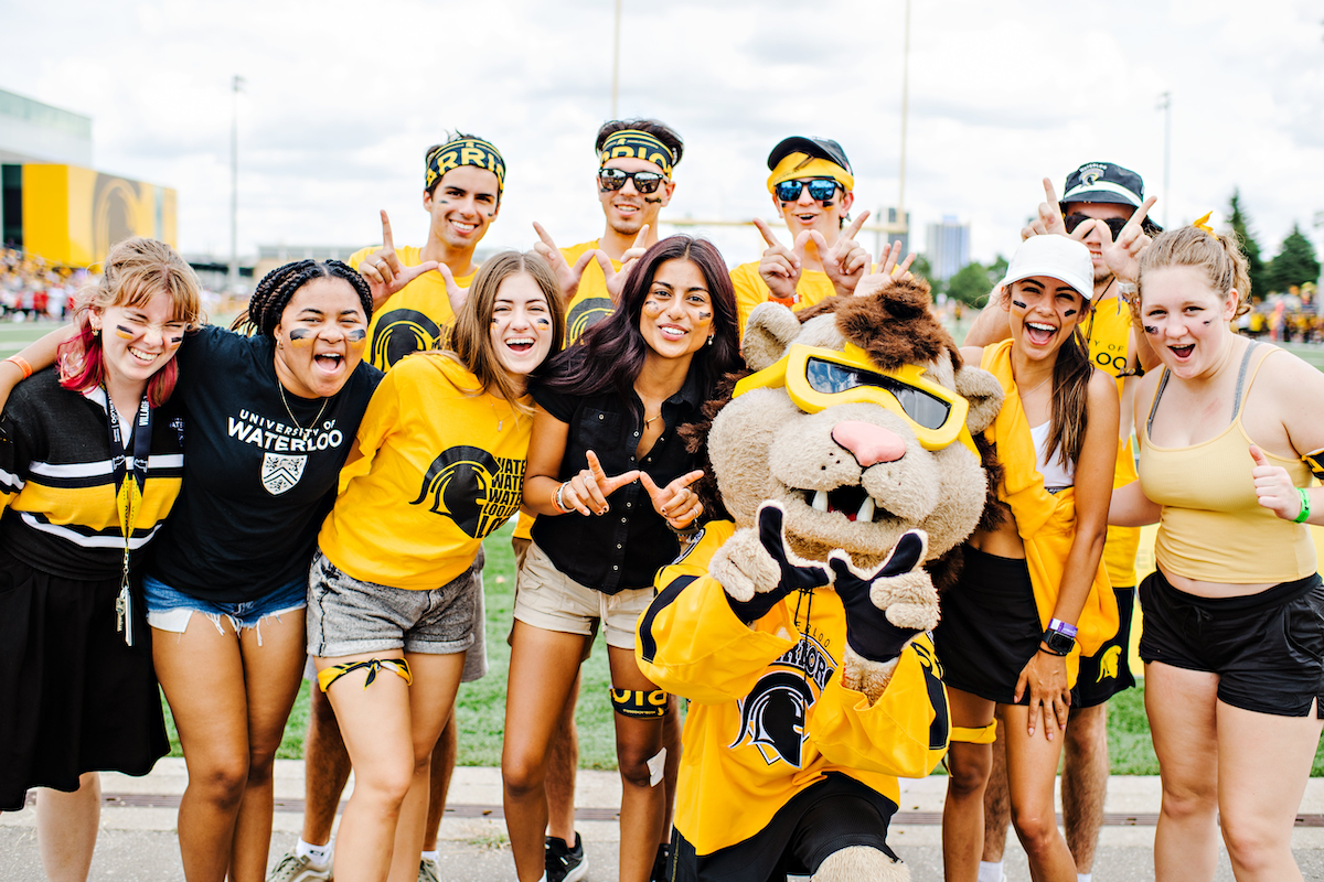 Students in Warriors gear make the "W" sign with their hands along with the King Warrior mascot.
