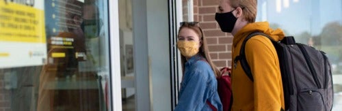 Masked students enter a campus building.