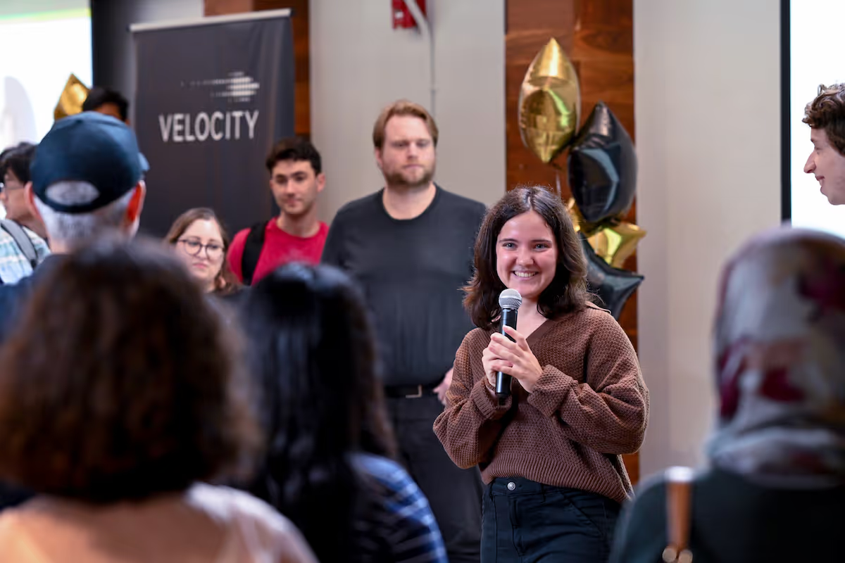 A woman holds a microphone while giving a presentation to her peers.