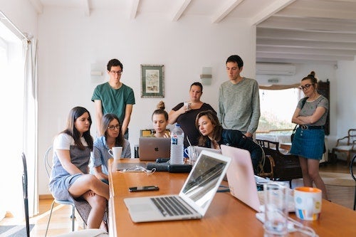 Young people gather together around a table with laptops.