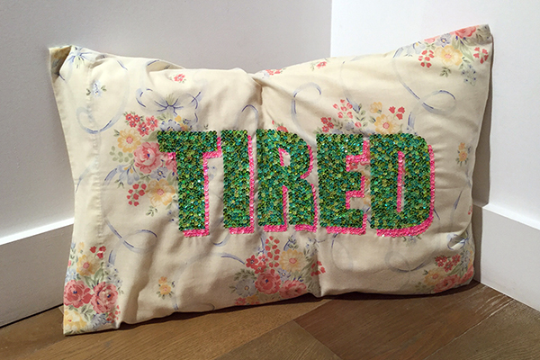 A throw pillow with the word "Tired" marked in green sequins.