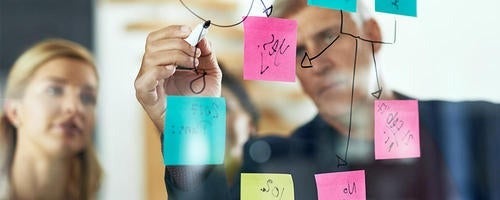 Two people write on a board covered with coloured sticky notes