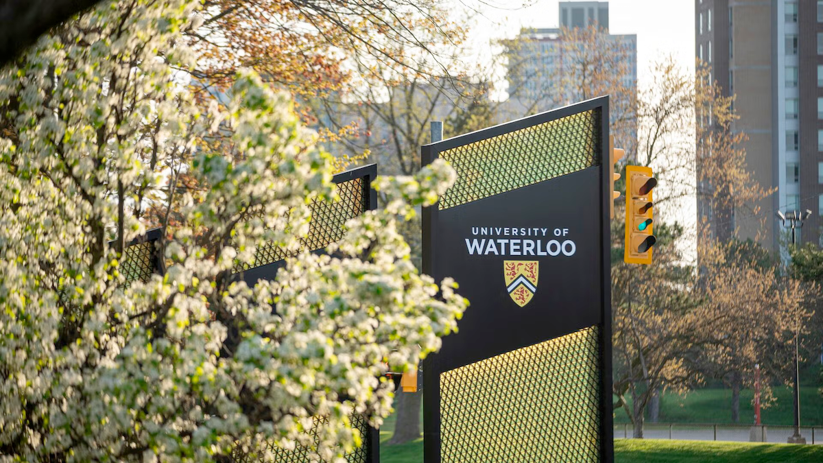 The Waterloo sign at the south campus entrance flanked by blossoming tree.