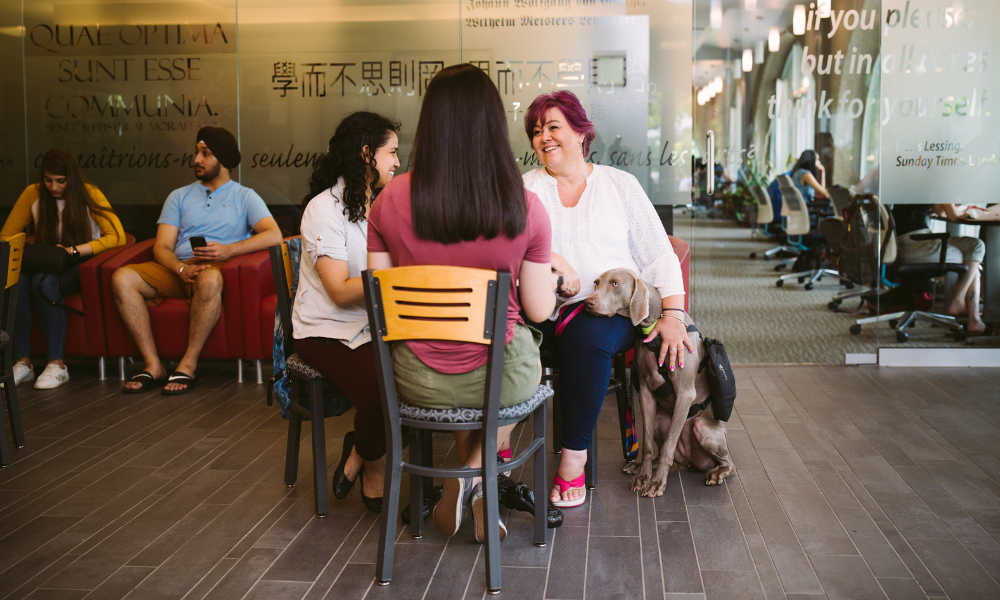 A woman and her service dog sits at a table conversing with friends.