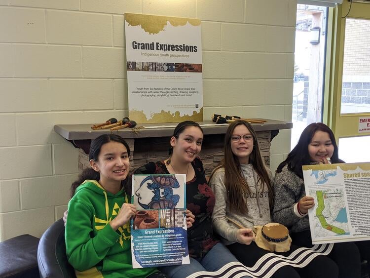 Youth from the Music for the Spirit and Indigenous Visual Arts program together with Elaine Ho, with posters and signage from the Grand Expressions in-person exhibit.