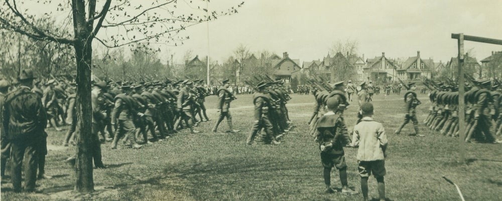 Members of the 118th Battalion, recruited in Kitchener, march as children look on.