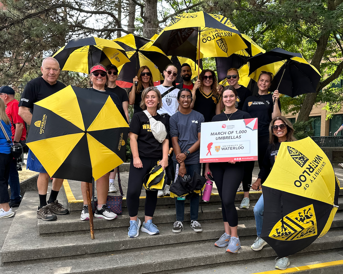 Waterloo March participants with their t-shirts and black and gold umbrellas outside South Campus Hall.