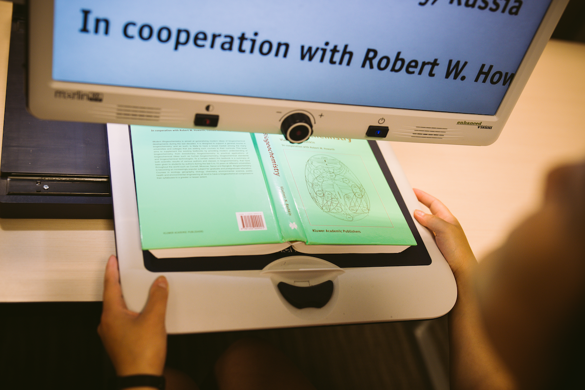 A textbook being scanned so that large print is available on a screen above.