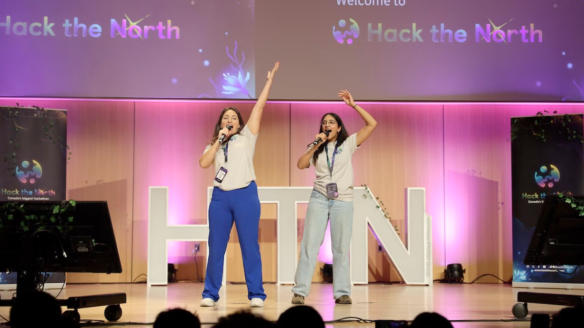 Two women with microphones hype up the crowd on the Hack the North stage.