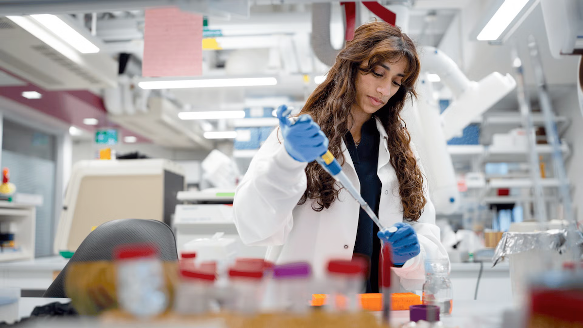 Yusra Kureshi wears a white lab coat while working in the lab.