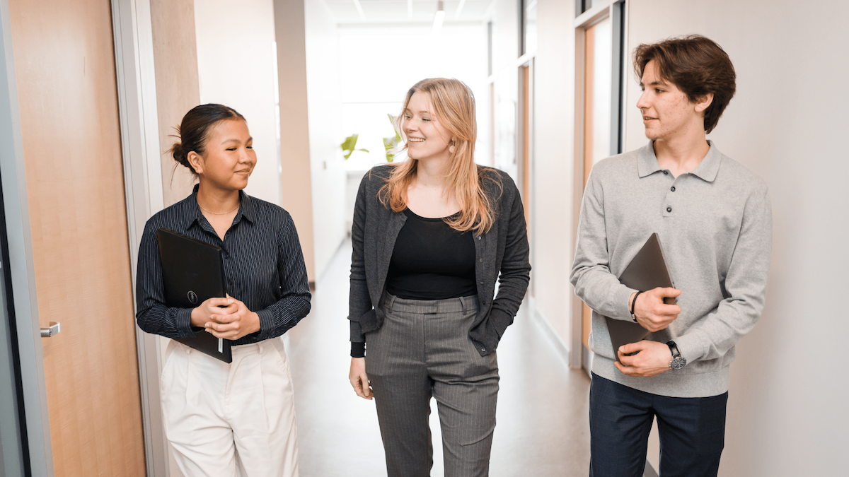 Three students walk down a hallway in conversation.