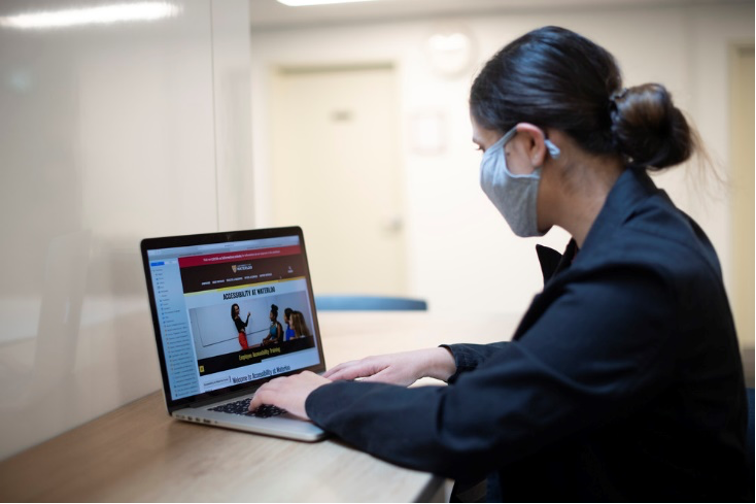 A masked person uses a laptop.