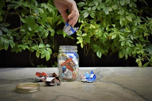 A hand drops a piece of waste into a mason jar full of plastic wrappers