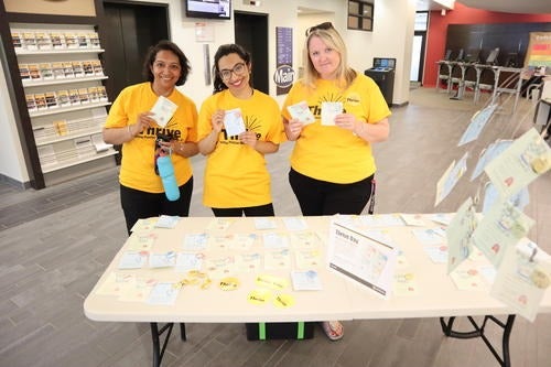 Three Thrive volunteers wearing yellow Thrive shirts at a sign-up table.
