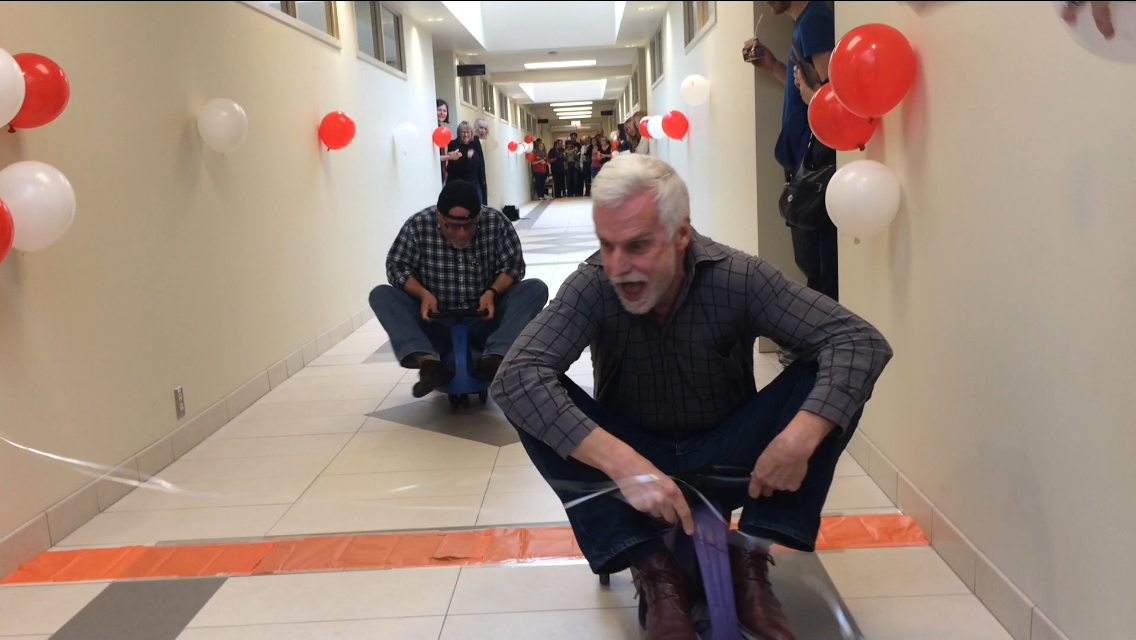 A hallway race. Two grown men on plasmacar bikes.