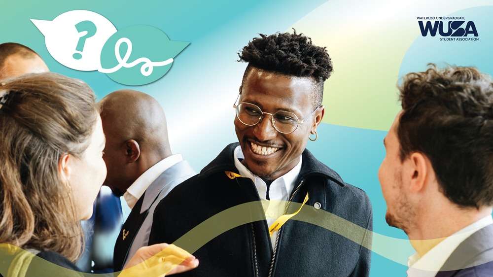 A smiling man with glasses speaks with two people.