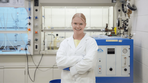 Allysa Greidanus wears a lab coat as she stands in a chemstry lab.