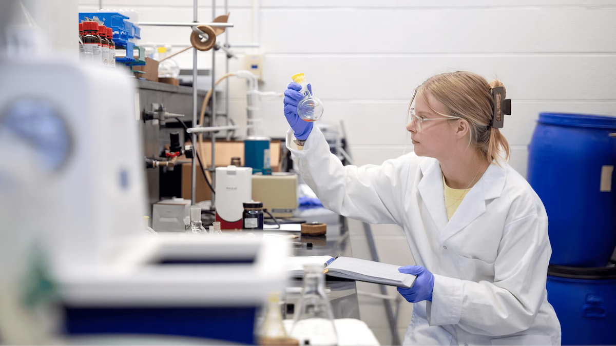 Allysa Greidanus wears gloves as she examines liquid in a bulbous flask.