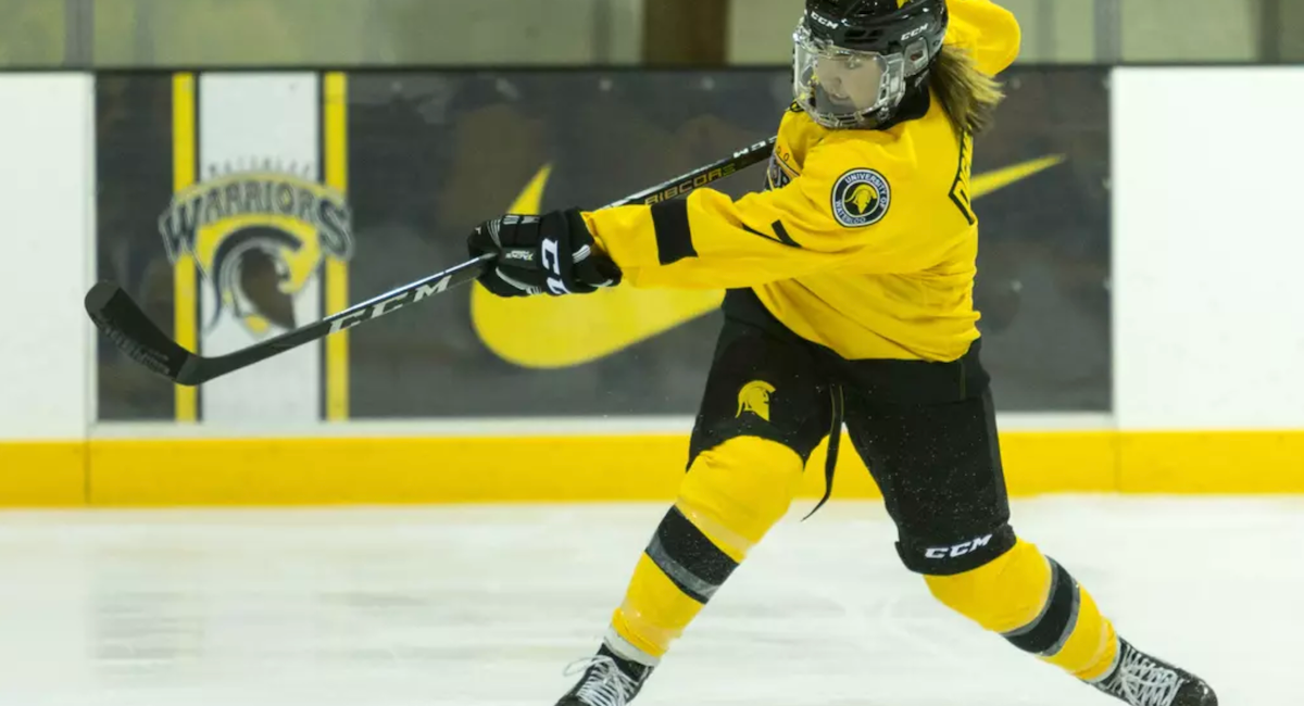 A member of the Women's Hockey team hits the puck with her hockey stick.