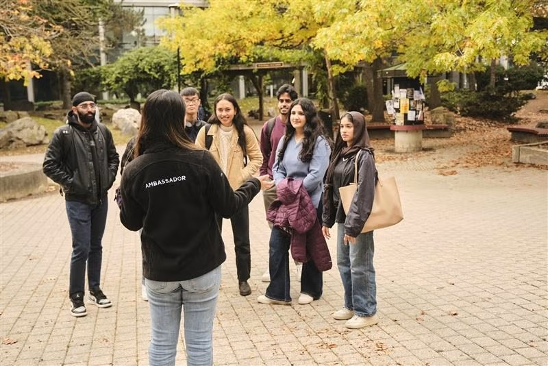 Students taking a tour of campus with the Peter Russell rock garden in the background.
