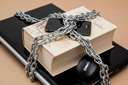 A laptop, hardcover book and smartphone locked together with heavy chains.