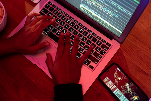 A person's hands typing on a laptop keyboard with a smartphone nearby.