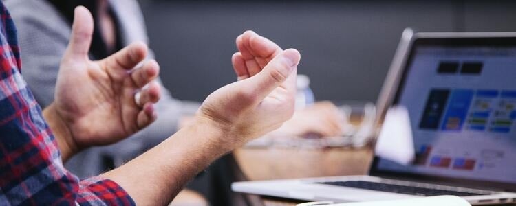 A close shot of gesturing hands with a laptop in the background.
