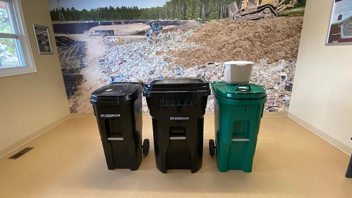 The Region of Waterloo's new black and green waste bins in front of a mural of a landfill.