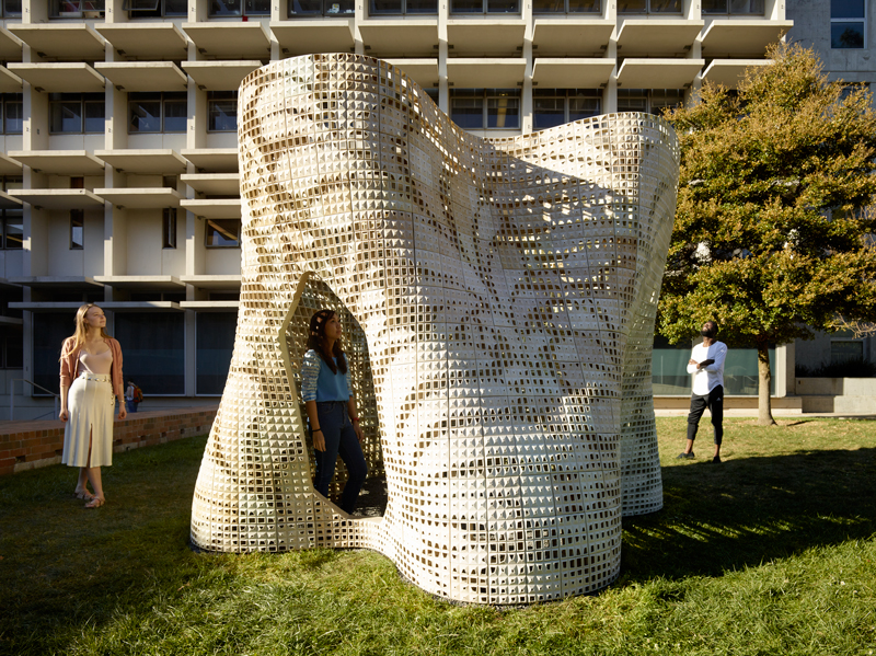 A 3D architectural design wtih people standing next to it.