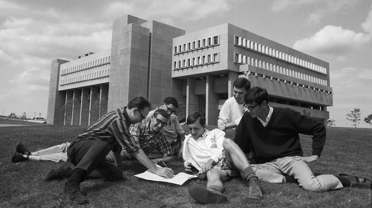 Students sit before the Mathematics and Computer Building, checking a printout.