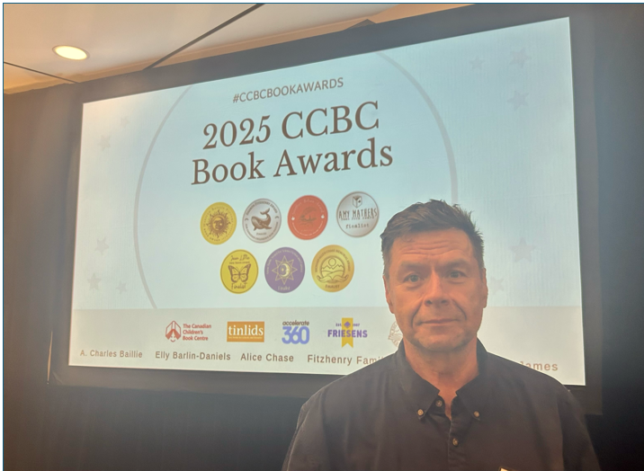 Mark Morton stands in front of the 2025 CCBC Book Awards sign.