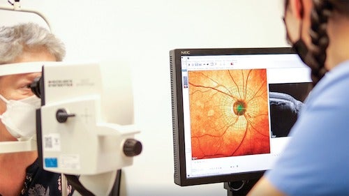 An optometrist performs a digital imaging scan on a patient showing a close-up of the person's eye.