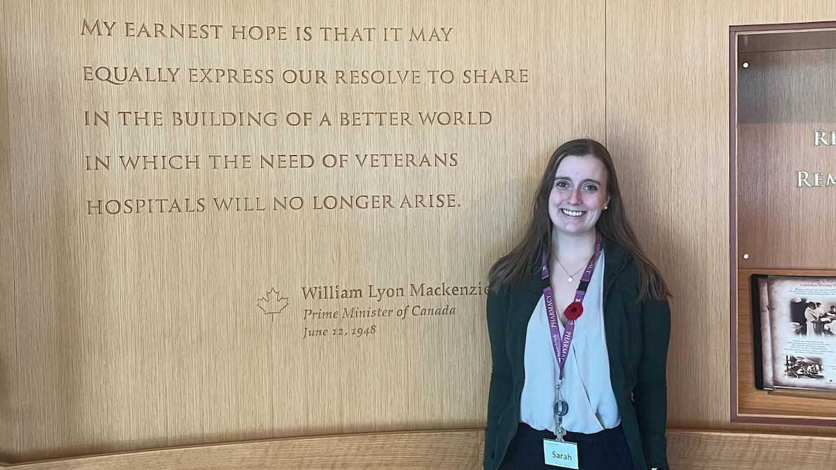 Sarah Fallis, wearing a poppy, stands next to a quote from William Lyon Mackenzie King.