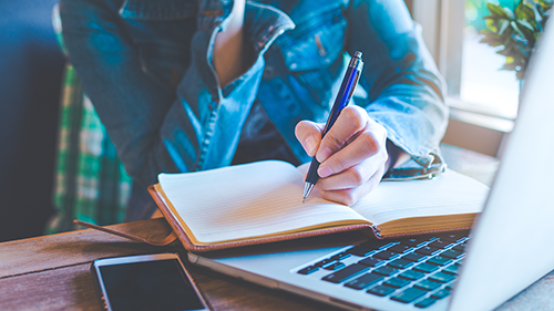 Close-up of hands writing in a notebook that is laying on a keyboard